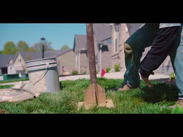 Workers preparing to dig hole with post hole digger for landscape installation in residential neighborhood