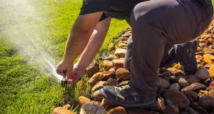 Technician adjusting a lawn sprinkler head near rock landscaping to ensure proper irrigation system performance in Cincinnati, OH