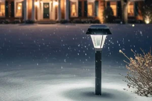 LED pathway light illuminating a snow-covered yard during falling snow in Northern Kentucky, highlighting cold-weather durability of outdoor landscape lighting near a residential home.