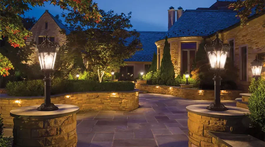 Elegant outdoor lighting with classic lamp posts and accent lights illuminating a stone pathway and landscaped garden in a luxurious nighttime setting.