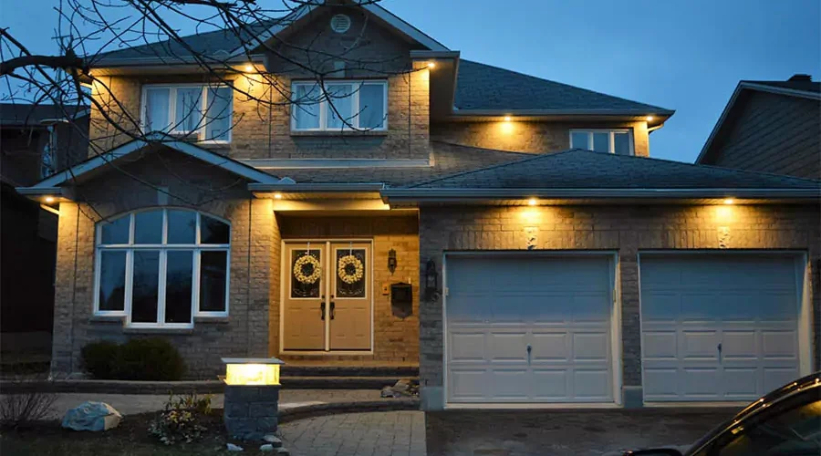 Elegant two-story home illuminated by warm, recessed outdoor lights along the roofline, highlighting the entryway and garage doors at dusk.