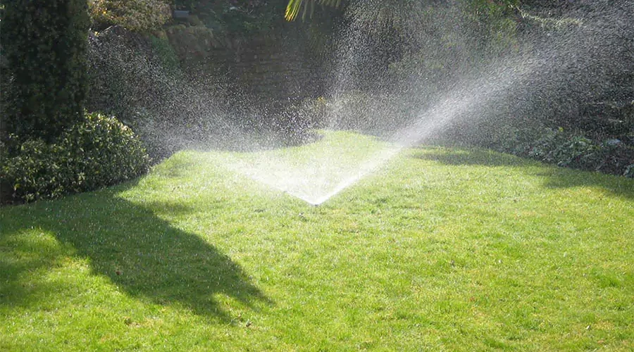 Sprinkler system watering a lush green lawn, demonstrating the benefits of adjusting watering schedules for maintaining healthy landscapes in Cincinnati during summer.