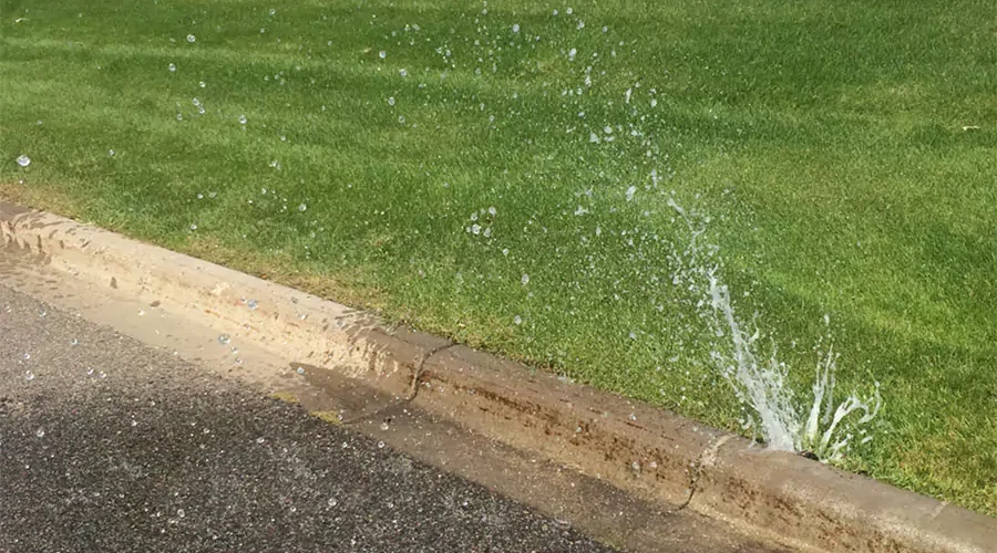 Broken sprinkler head leaking water onto a street curb in Cincinnati, showing common irrigation system problems caused by low water pressure.