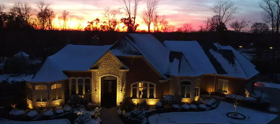 Sun rising with a view of beautiful outdoor lighting on a house that covers snow in Milford